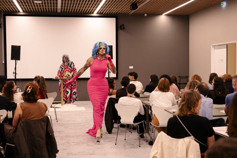 Une animatrice drag queen avance au milieu du public pour animer le bingo drag